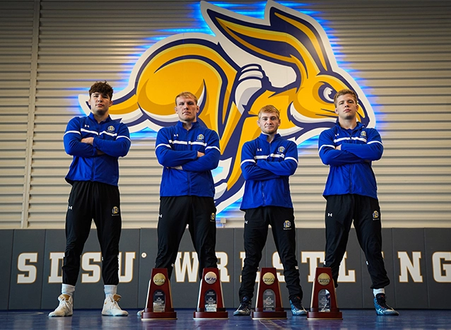 4 members of the SDSU wrestling team stand tough behind their NCAA trophies.