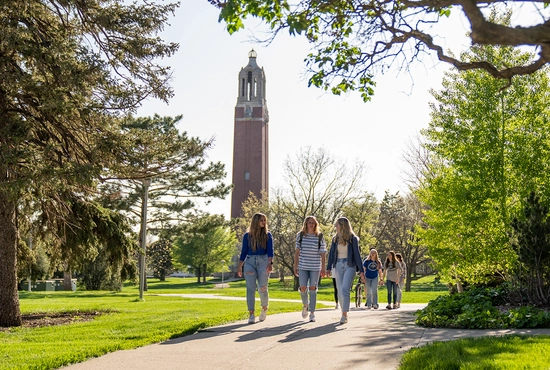 Three students walking on campus with the Coughlin Campanile in the distance.