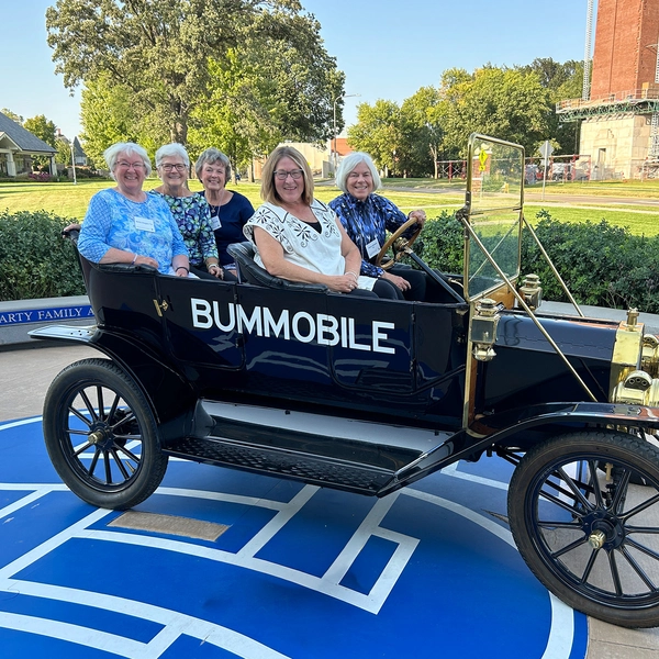 Five SDSU Class of 1974 women smile while sitting in the Bummobile outside of the SDSU Alumni Center.