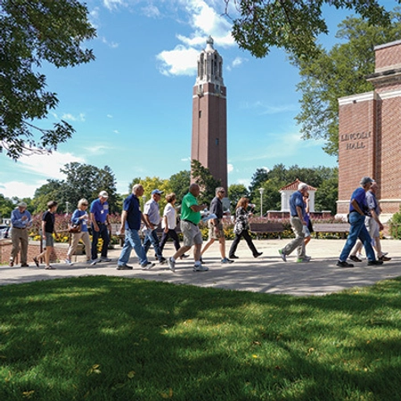 A group of people taking a walk along a campus pathway under a clear blue sky.