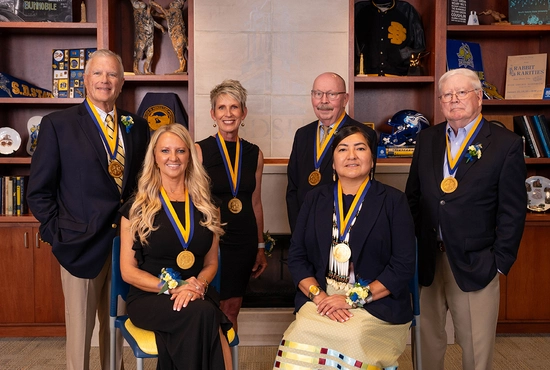 The six 2025 Distinguished Alumni honorees smile together in the Jensen Smith Board Room.