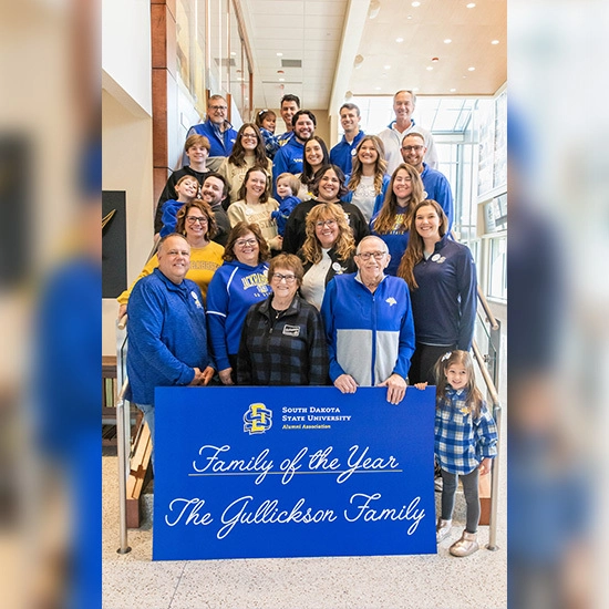 The Gullickson family smiles together on a set of stairs holding a "family of the year" sign
