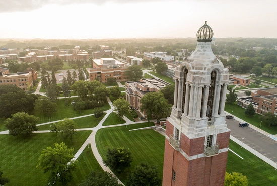 Aerial view of the SDSU campus featuring the top of the campanile surrounded by lush green lawns and brick buildings under a hazy sky.