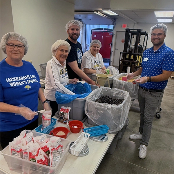 Group of five people volunteering to put together meal packets.