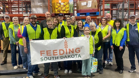 West River Jacks alumni chapter members stand together holding a large Feeding South Dakota sign after volunteering.