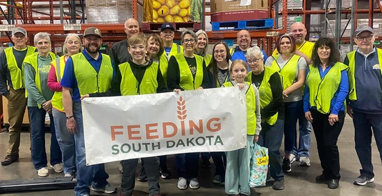 West River Jacks alumni chapter members stand together holding a large Feeding South Dakota sign after volunteering.