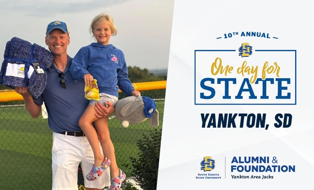 A smiling man carries his young daughter beside a baseball field and a graphic for the 10th annual One Day for STATE fundraiser in Yankton, SD.