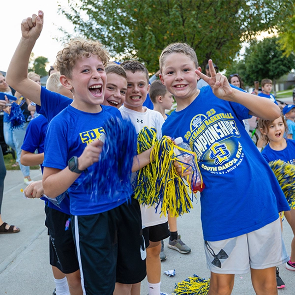 Group of young boys all dressed in Jackrabbit gear excitedly cheering and holding up pom poms.
