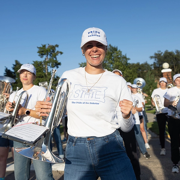 Member of a the Pride of the Dakotas smiles and dances holding an instrument during a performance