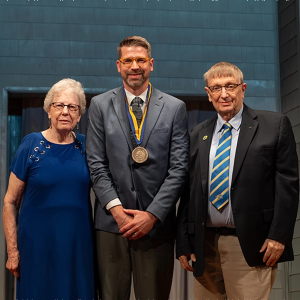 New endowed faculty member smiles while standing in the middle of the two donors who started the endowment.