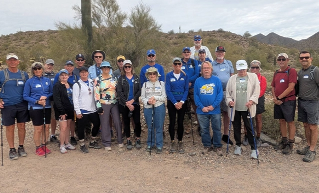 A group of hikers, wearing casual outdoor clothing and hats, stands on a hiking trail.