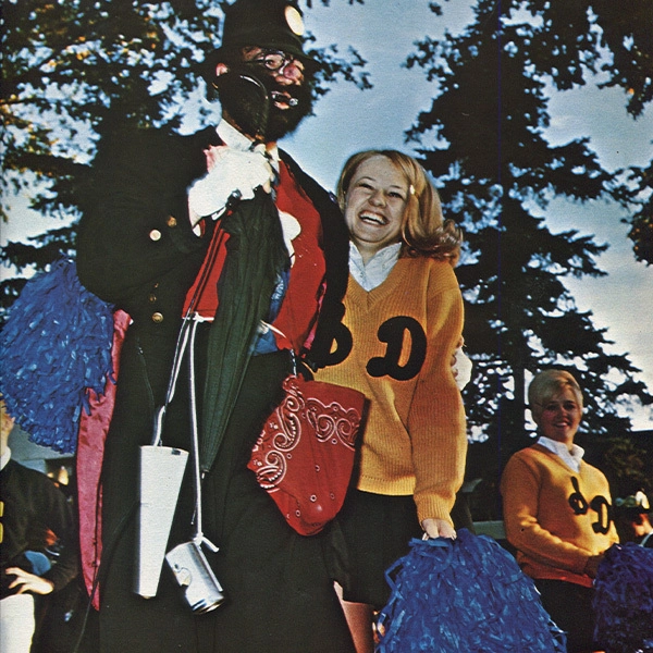 A historic photo of a woman smiling in a yellow SDSU sweater, standing next to Weary Wil.