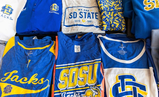 An array of blue and yellow SDSU-themed apparel being neatly displayed on a table.