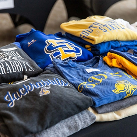 A variety of neatly folded SDSU shirts sitting on a table.
