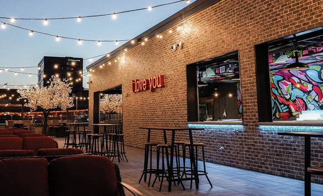 Rooftop bar at dusk with string lights, brick walls, and colorful graffiti.