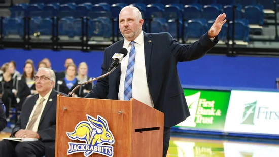 A photo of SDSU Athletic Director Justin Sell speaking from behind a podium in First Bank & Trust Arena.