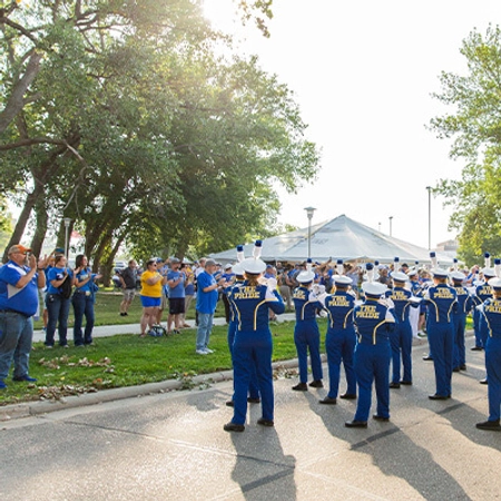 The Pride of the Dakotas Marching Band playing on the street while facing tailgate spectators.