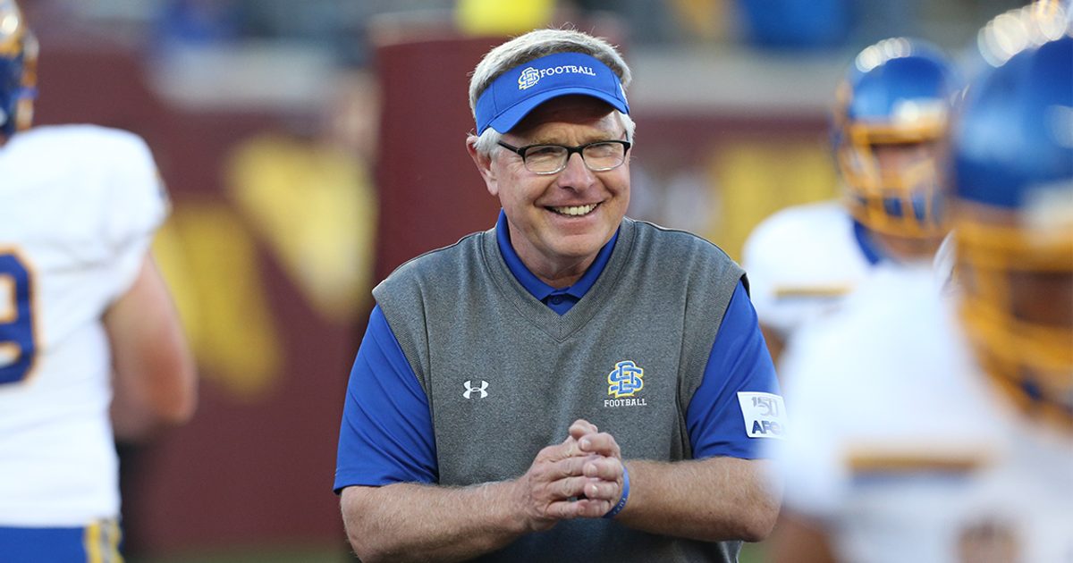 Coach Stig smiles during a SDSU Football game with a few players blurred around him.