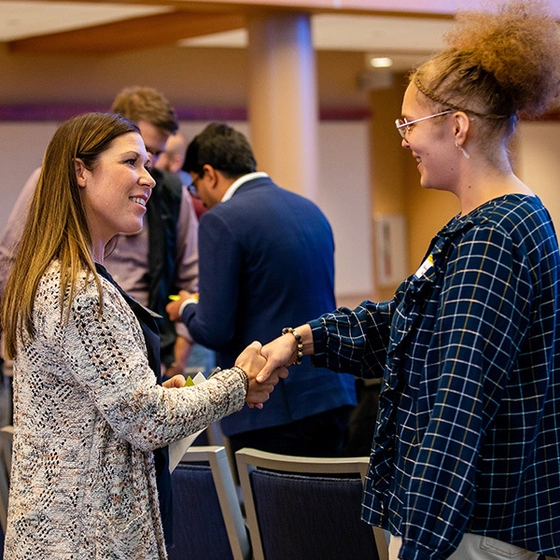A photo of a mentor shaking hands with their student mentee at an event inside of the SDSU Alumni Center.
