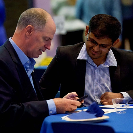 A photo of a mentor and mentee sitting at a table looking at a phone.