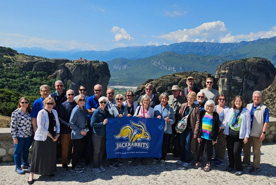 A group photo in front of a beautiful landscape while holding up a Jackrabbits banner.