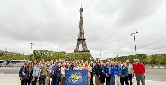 A large group of Jackrabbits traveling together pose for a group photo in front of the Eiffel Tower in Paris.