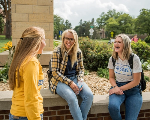 Three SDSU students sit outside chatting between classes