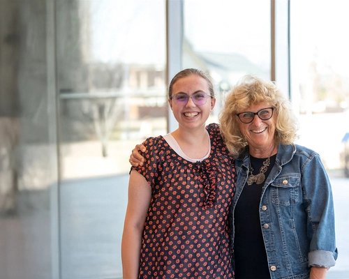 An woman her arm around a younger woman, both smiling.