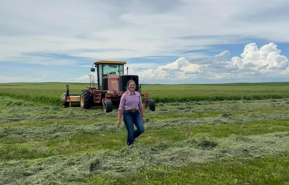 Abby stands in a field with a beautiful blue sky and a tractor behind her.