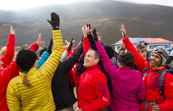 Dick Deming high-fiving others in a group at the base of a mountain