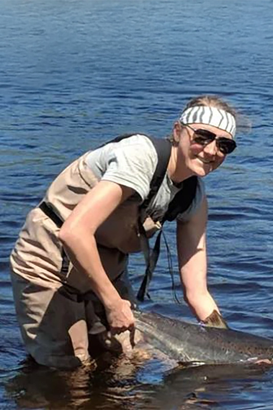 A girl standing in shallow water holding a fish