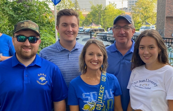 Marc and Julie Mooney standing with their three kids at a football game.