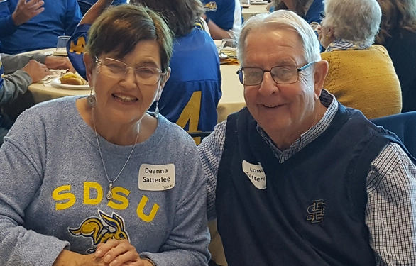 Lowell and Deanna Satterlee, sitting at a table, smiling, in SDSU clothes.
