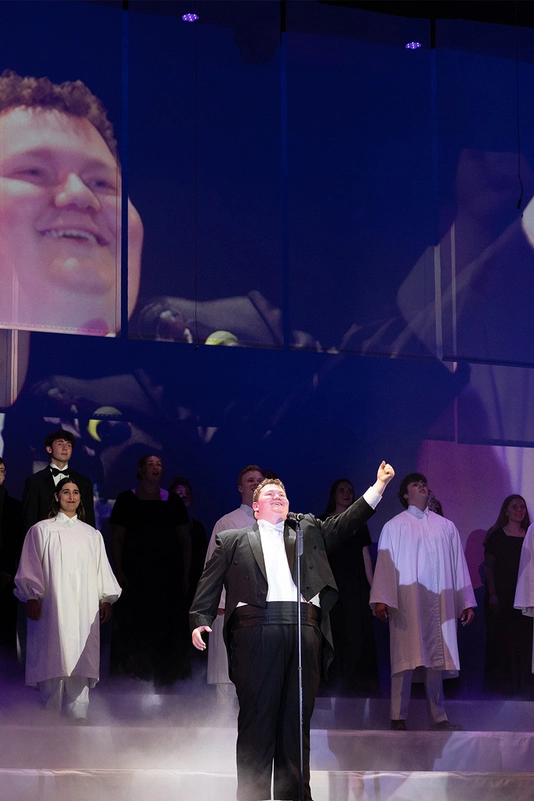 A man singing on stage with a choir