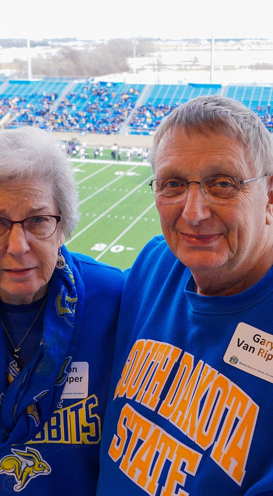 Sharon and Gary Van Riper smile for camera with the SDSU football field in the background