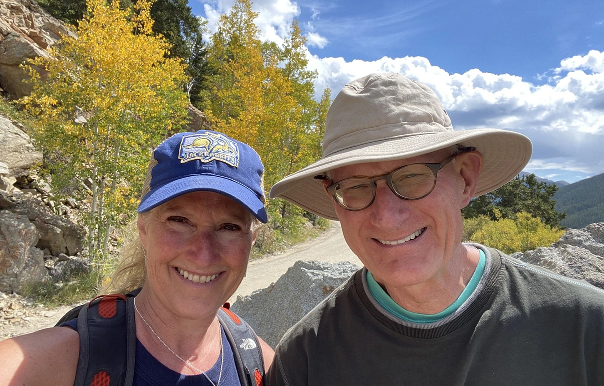 Rebecca Kurtz and Steve Schwanke smile at the camera while on a hike in a mountain area
