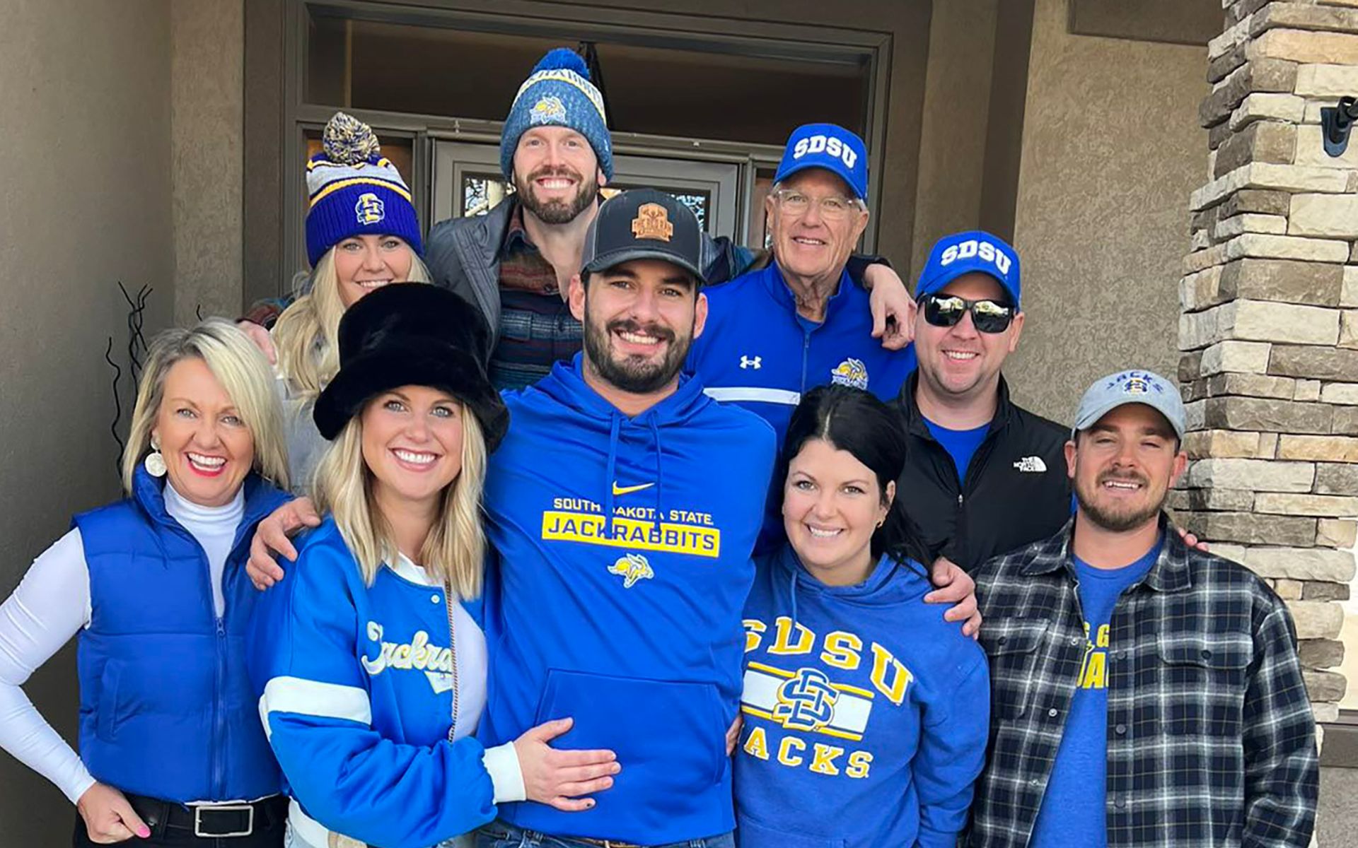 Helsper family stands on the front porch of their home smiling and all wearing Jackrabbit gear