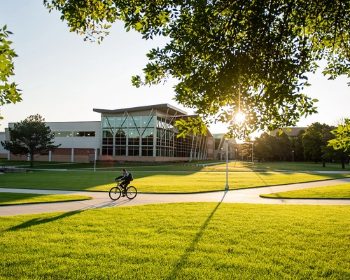 Sunny day showing Campus Green and the Miller Wellness Center in the background and a biker on the sidewalk