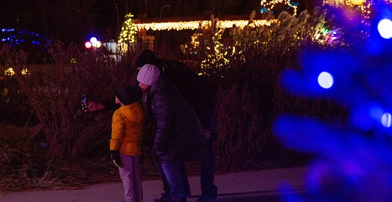 Young family taking a selfie photo with the glowing lights from Garden Glow behind them.