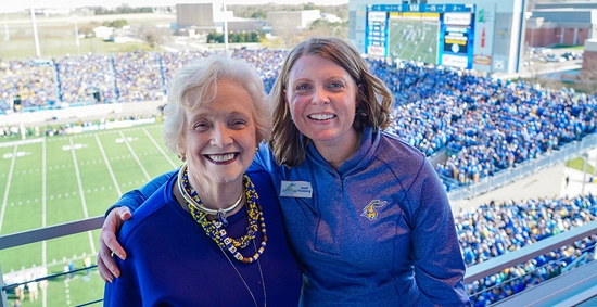 Peggy Gordon Miller and Andi Fouberg smiling for the camera at a SDSU football game, all dressed in blue and Jackrabbit gear.