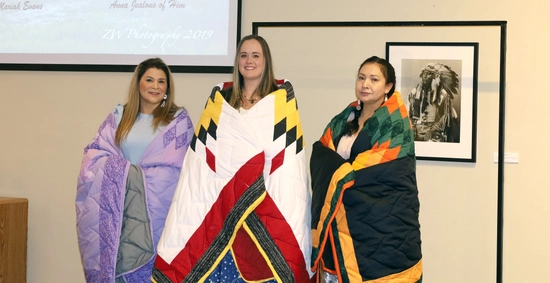 3 nursing students wrapped in star quilts at their honoring ceremony. Anna Jealous of Him is pictured far right.