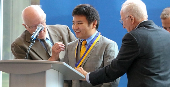 Dr. Liu smiling while receiving his medallion from Duane Sander and Al Kurtenbach.