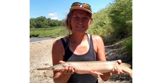 erin peterson smiles outdoors proudly holding a fish in her hands