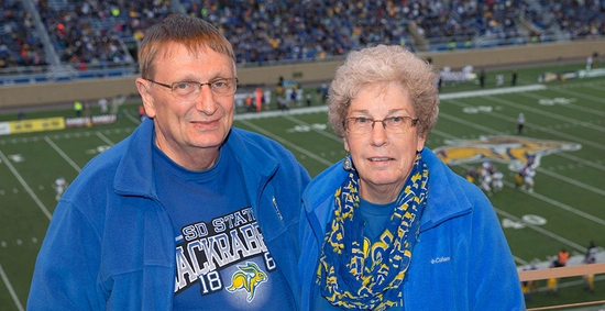Gary and Sharon Van Riper smile for camera with the SDSU football field in the background