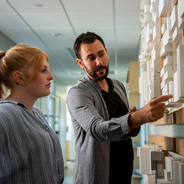 Male architecture professor and a female student look at a cityscape view hanging on the wall.