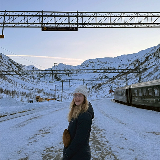 A student poses in front of a snowy landscape in Sweden for the choir trip.