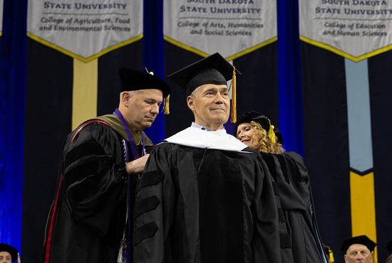 Dick Deming receiving his honorary doctorate degree at the 2025 commencement ceremony at South Dakota State University