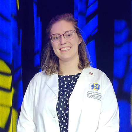 Emily smiles with her pharmacy white coat on.