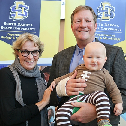 Brian and Denise Aamlid smile with the grandson who's wearing a football onesie