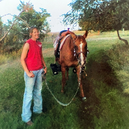 Stephanie Andersen Williams smiles with a brown horse beside her